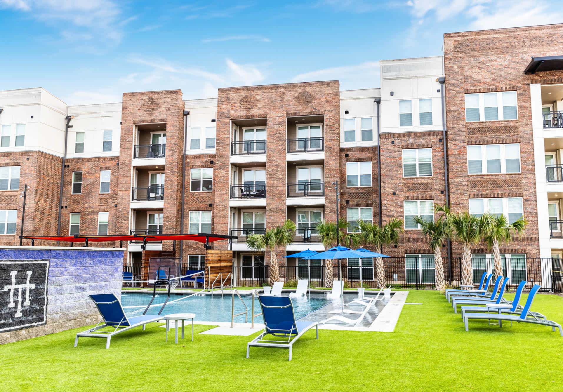 An outdoor pool with lounge chairs and tables in front of an apartment